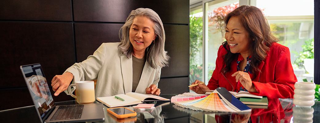 Image of female hearing aid wearer pointing to her laptop screen while speaking with a female client